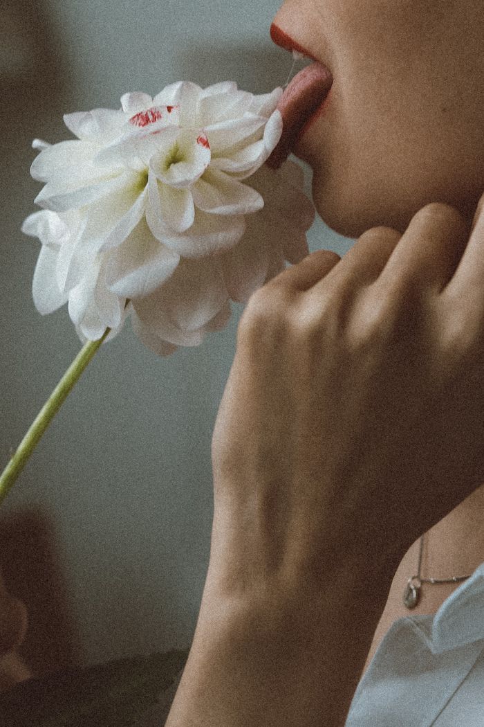 A dramatic close-up of a woman gently touching a white flower with her lips.
